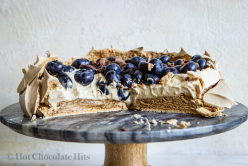 coffee pavlova topped with cream and blueberries on cake stand, cut to show interior