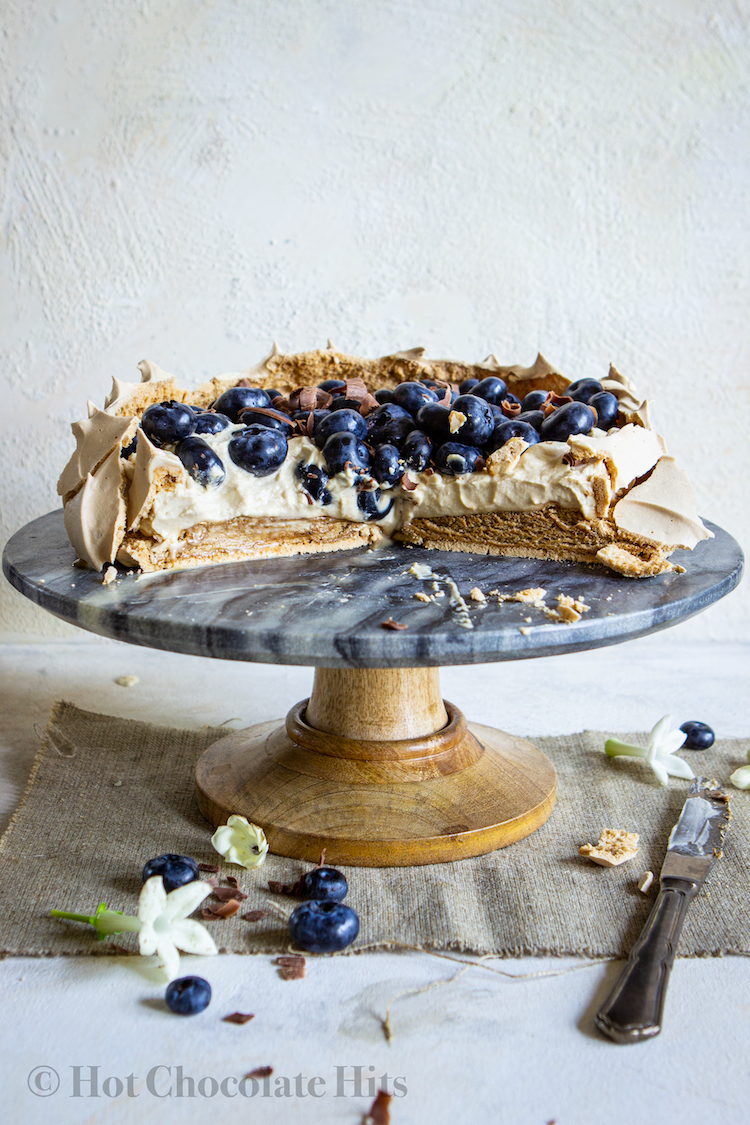 coffee pavlova topped with cream and blueberries on cake stand, cut to show interior