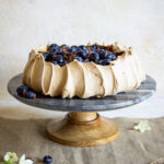 coffee pavlova topped with cream and blueberries on cake stand