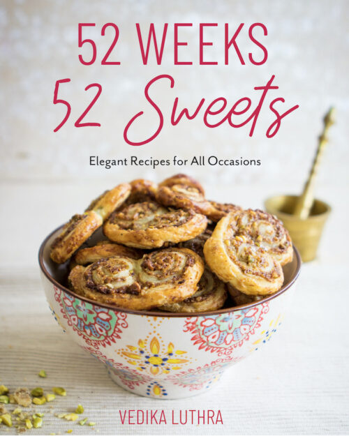 Picture of the cover of the cookbook 52 weeks 52 sweets. It shows a bowl of palmier cookies with crushed pistachios in the foreground and a gold mortar and pestle in the background.
