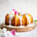a picture of a vanilla bundt cake topped with white lemon glaze and decorated with fresh flowers.