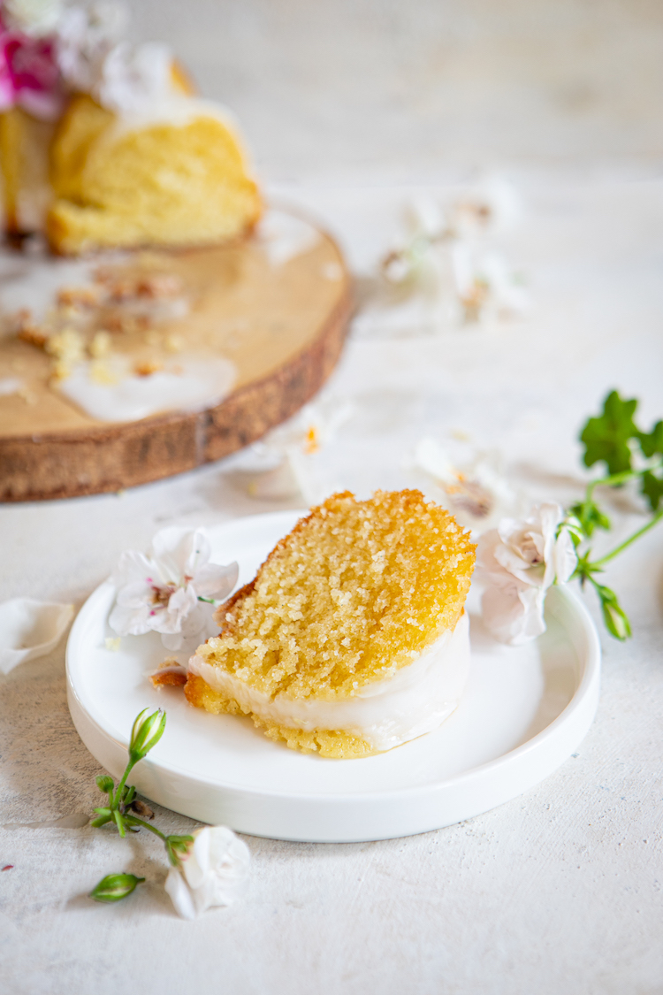 a picture of a slice of vanilla bundt cake topped with white lemon glaze and decorated with fresh flowers.