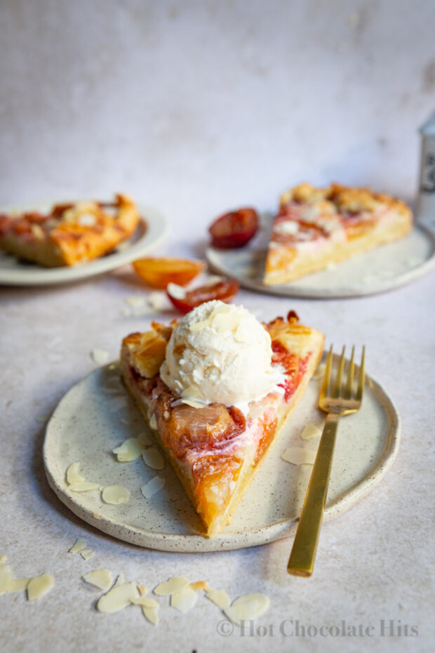 A piece of the rustic plum tart (center) with a scoop of vanilla ice cream. More pieces are pictured in the background.