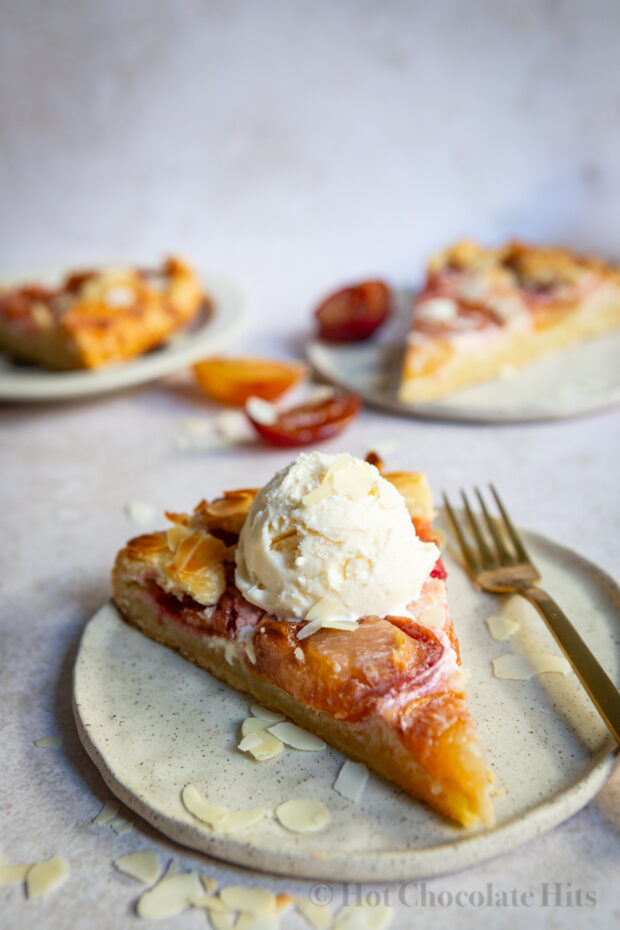 A piece of the rustic plum tart (center) with a scoop of vanilla ice cream. More pieces are pictured in the background.